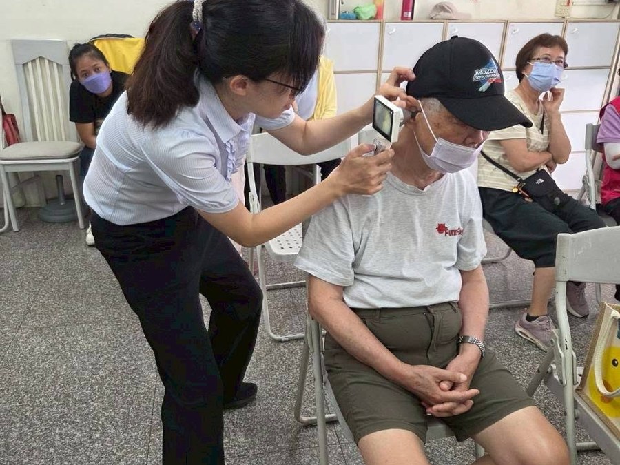 上聆人員在社區據點為一位長者做聽力檢查,旁邊還有其他等候的長輩